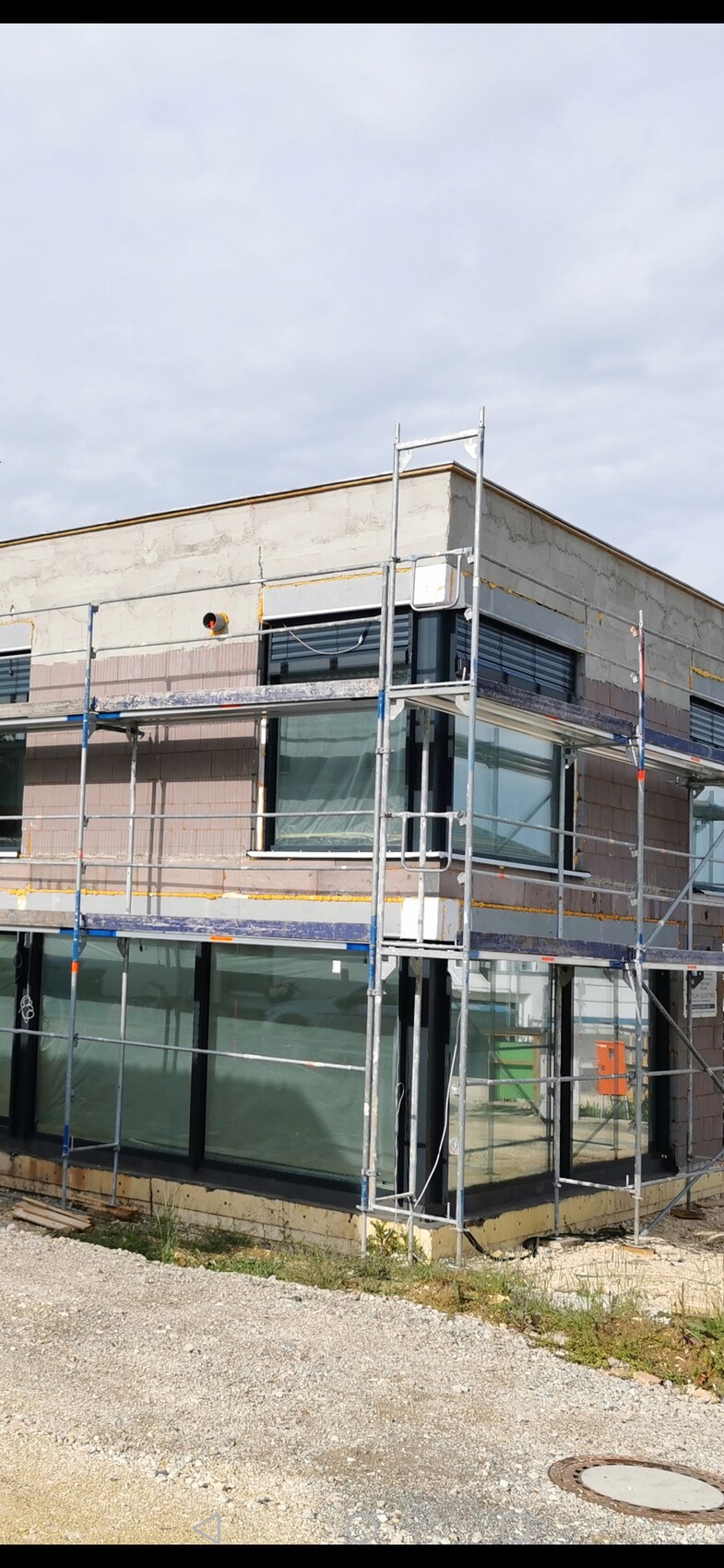 Baugerüst um modernes Geschäftshaus mit großen Glasfenstern, unvollständige Außenfassade.