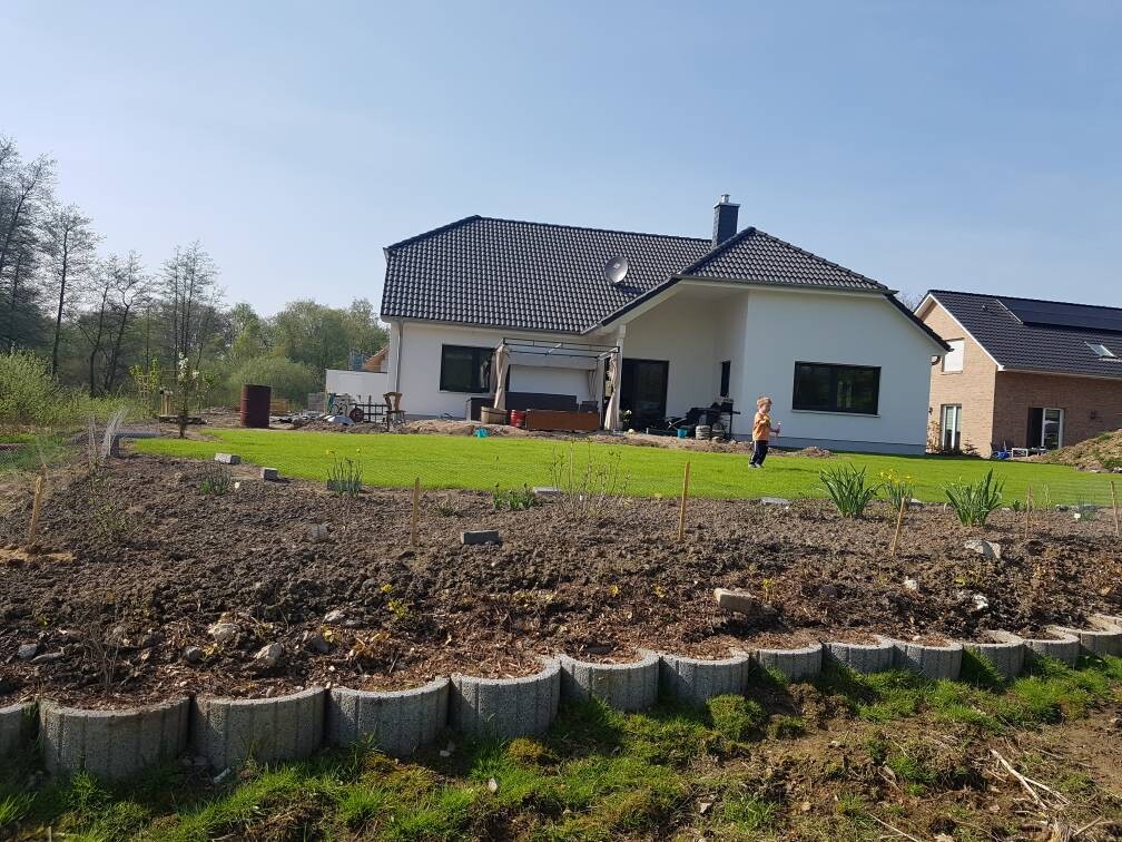 Einfamilienhaus mit grünem Garten, Terrasse und Baugebiet im Hintergrund