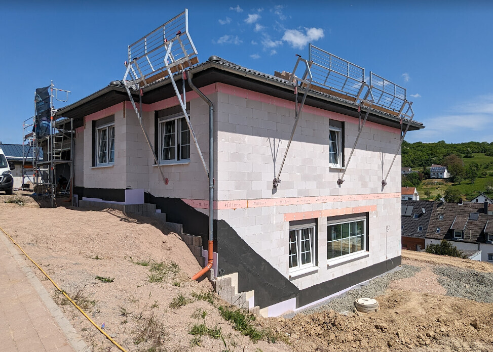 Zweistöckiges Haus im Bau mit Gerüst, blauer Himmel und Nachbarschaft im Hintergrund.