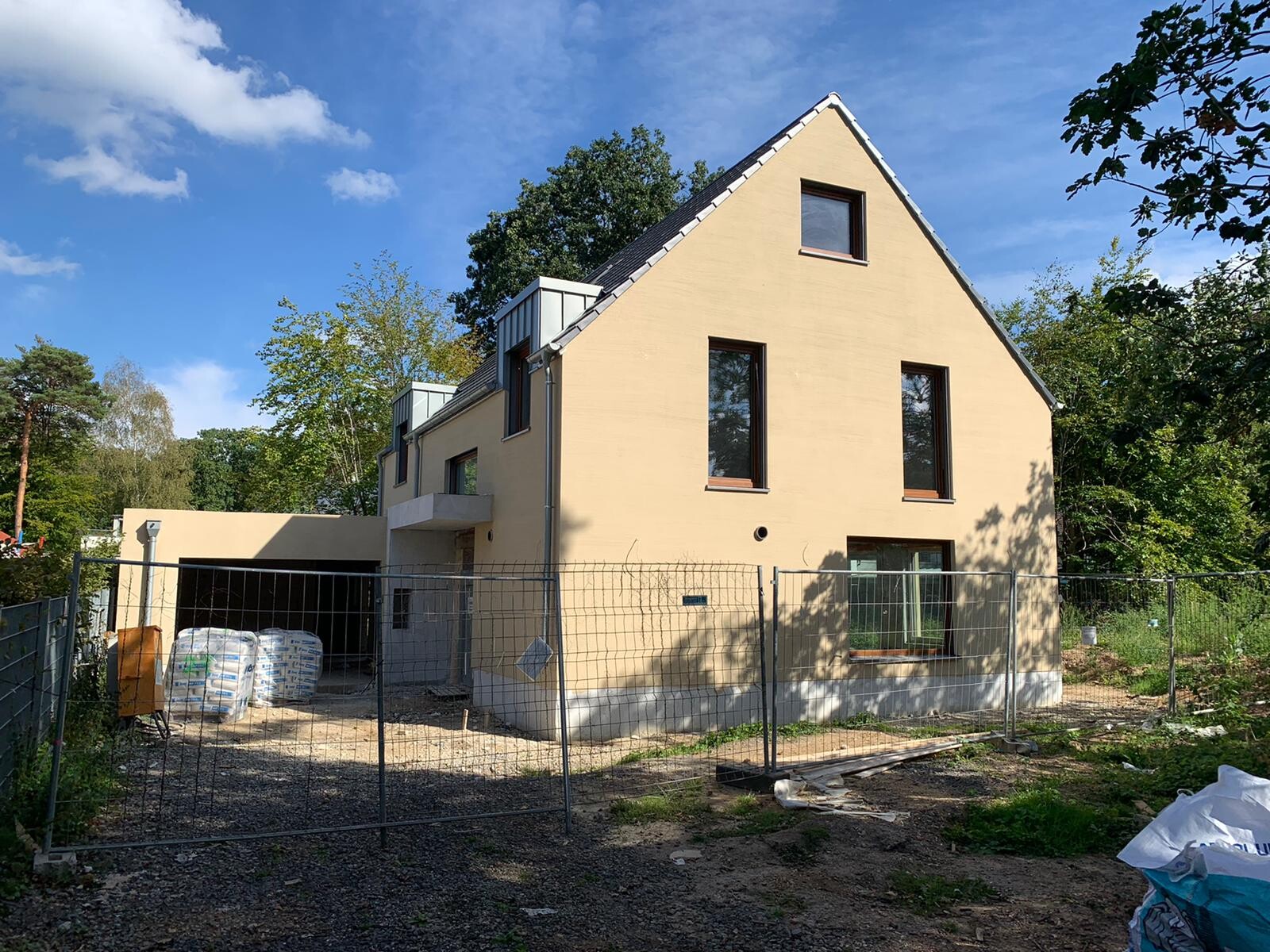 Beige Neubauhaus mit Dachfenstern, Bauzaun und Bauplatz auf Baustelle
