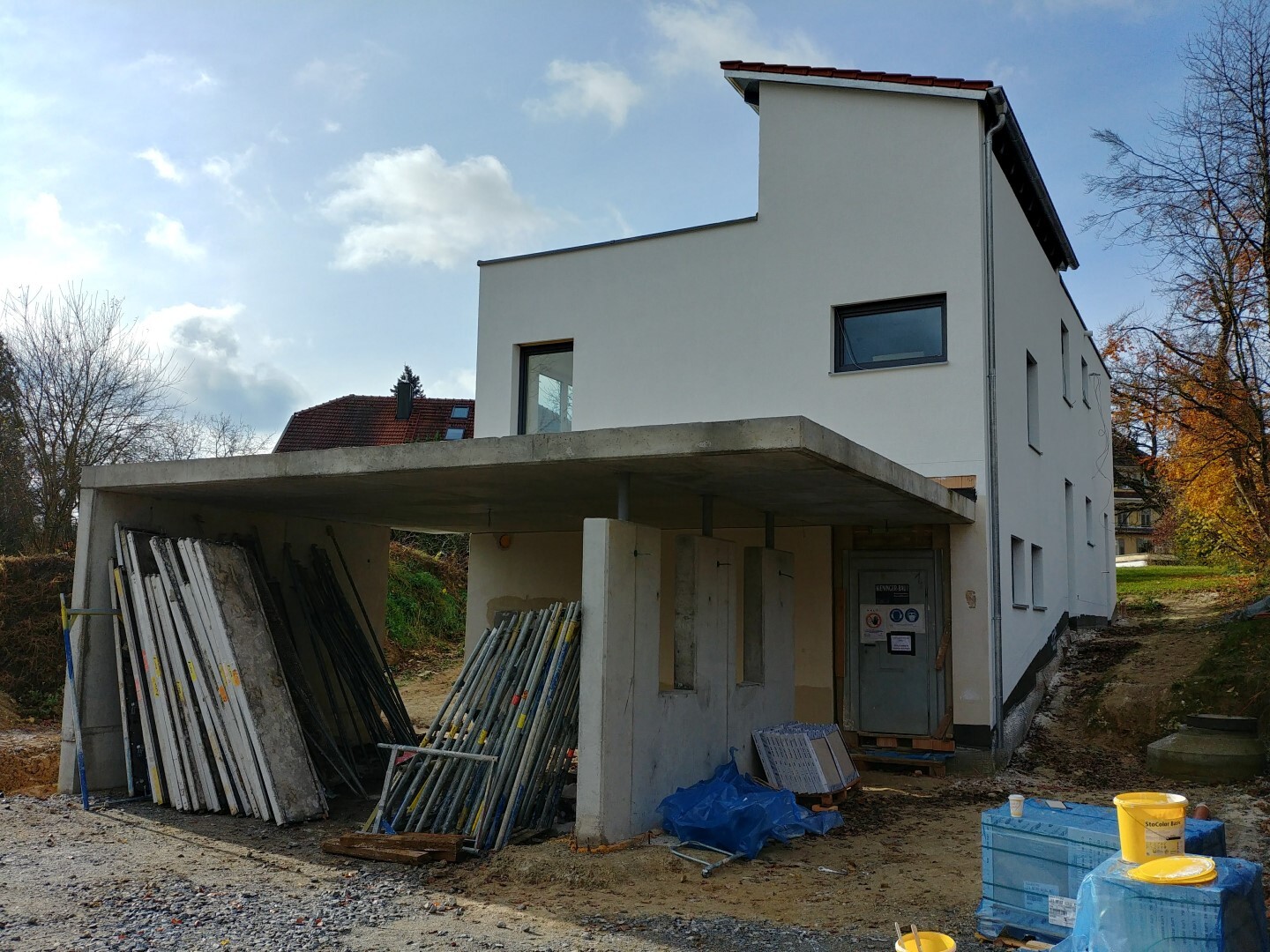 Modernes weißes Haus im Bau; Carport mit Materialstapeln, Gerüstteilen und Bauzubehör.