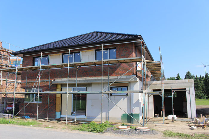 Zweistöckiges Wohnhaus aus Ziegeln im Rohbau, mit Gerüst rundum und Bauarbeiten.