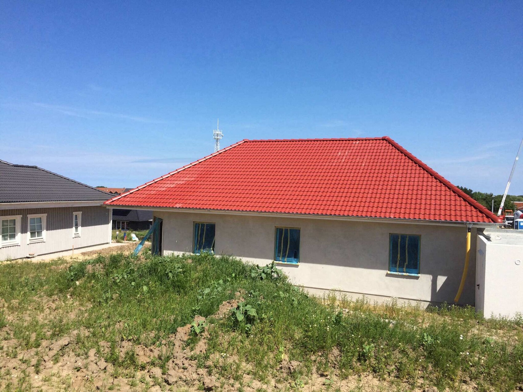 Neubau mit rotem Ziegeldach, hellen Wänden und Gras vor blauem Himmel