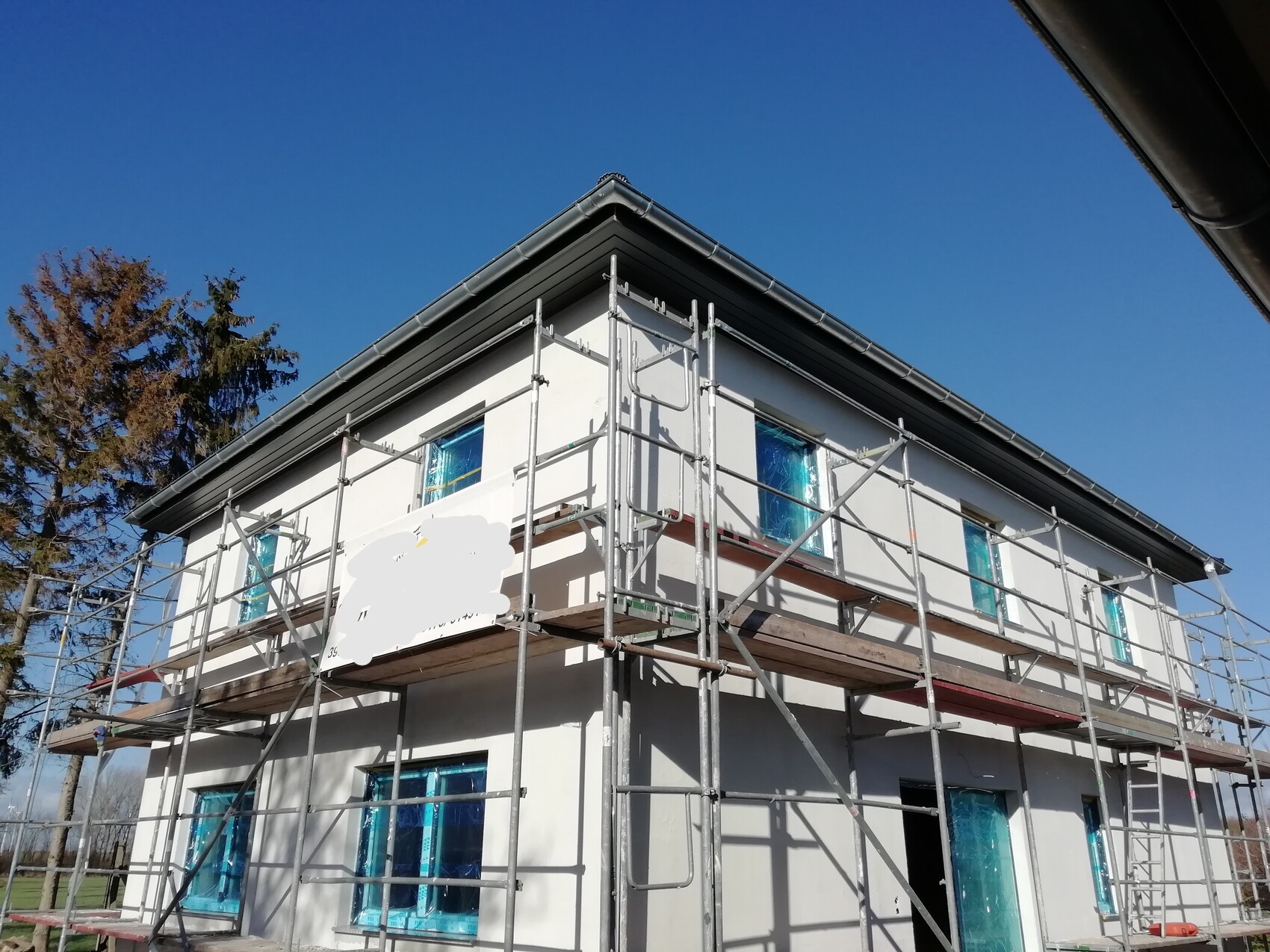 Zweistöckiges Haus mit Baugerüst, blaue Fensterabdeckungen, weiße Fassade, blauer Himmel
