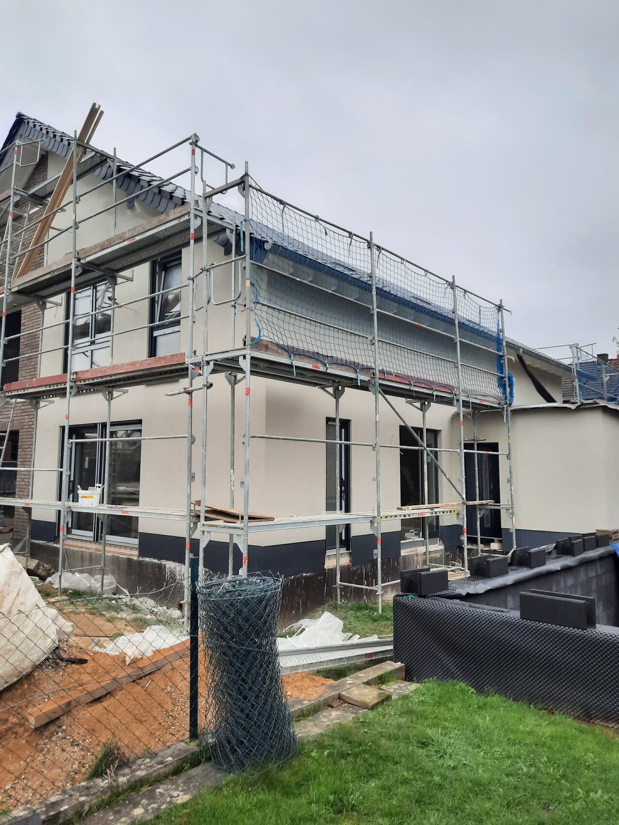 Zweistöckiges Haus im Bau mit Gerüst, Sicherheitsnetzen und Baumaterialien auf der Baustelle