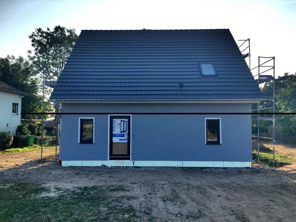 Neues zweistöckiges Haus im Rohbau, blaue Fassade, Dachziegel, Gerüst ringsum.