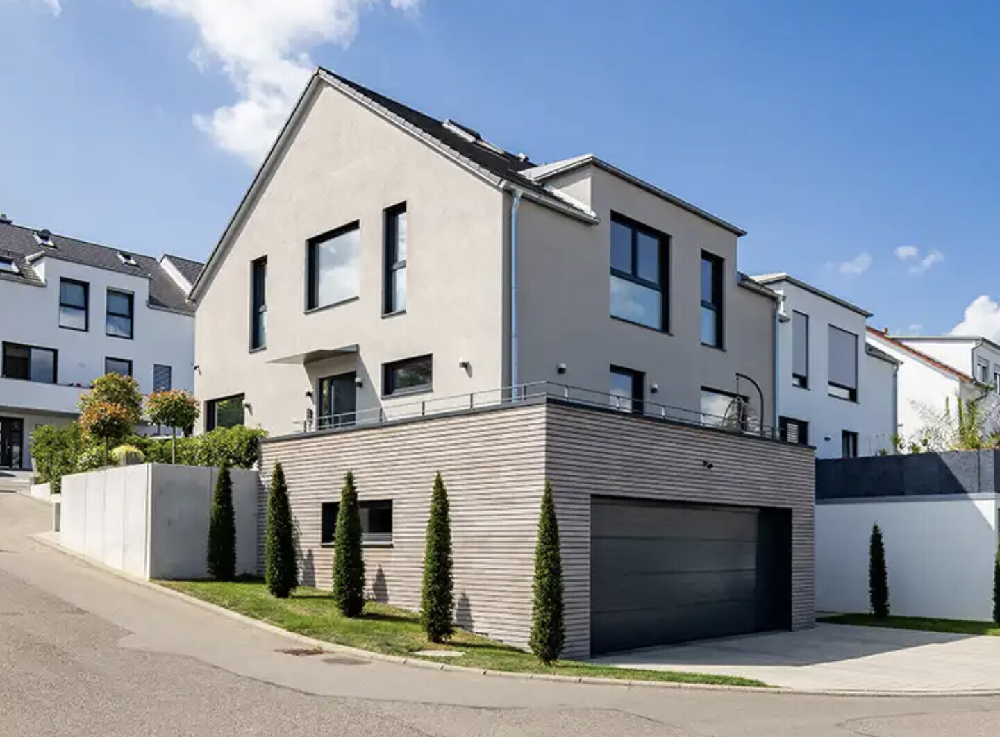 Moderne Wohnhäuser mit Garage, großen Fenstern und geschmackvoll bepflanzter Zufahrt.