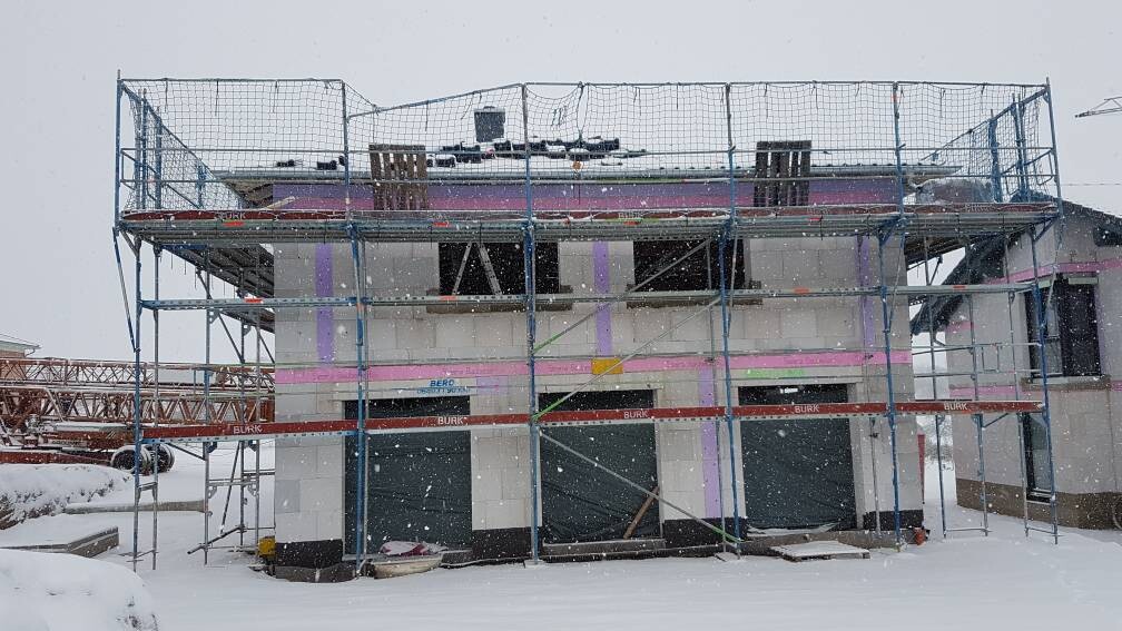 Winterliches Baugerüst um ein zweistöckiges Haus im Bau; Schnee fällt.