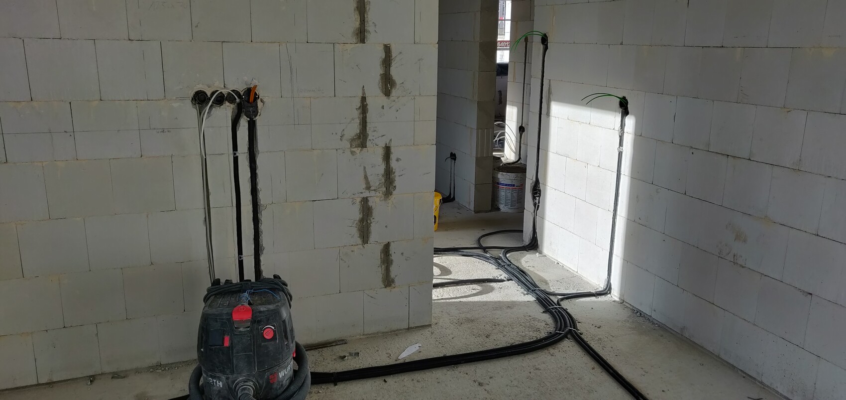 Baustelle im Innenraum mit weißen Blöcken, sichtbaren Kabeln, Schläuchen und Staubsauger am Boden.