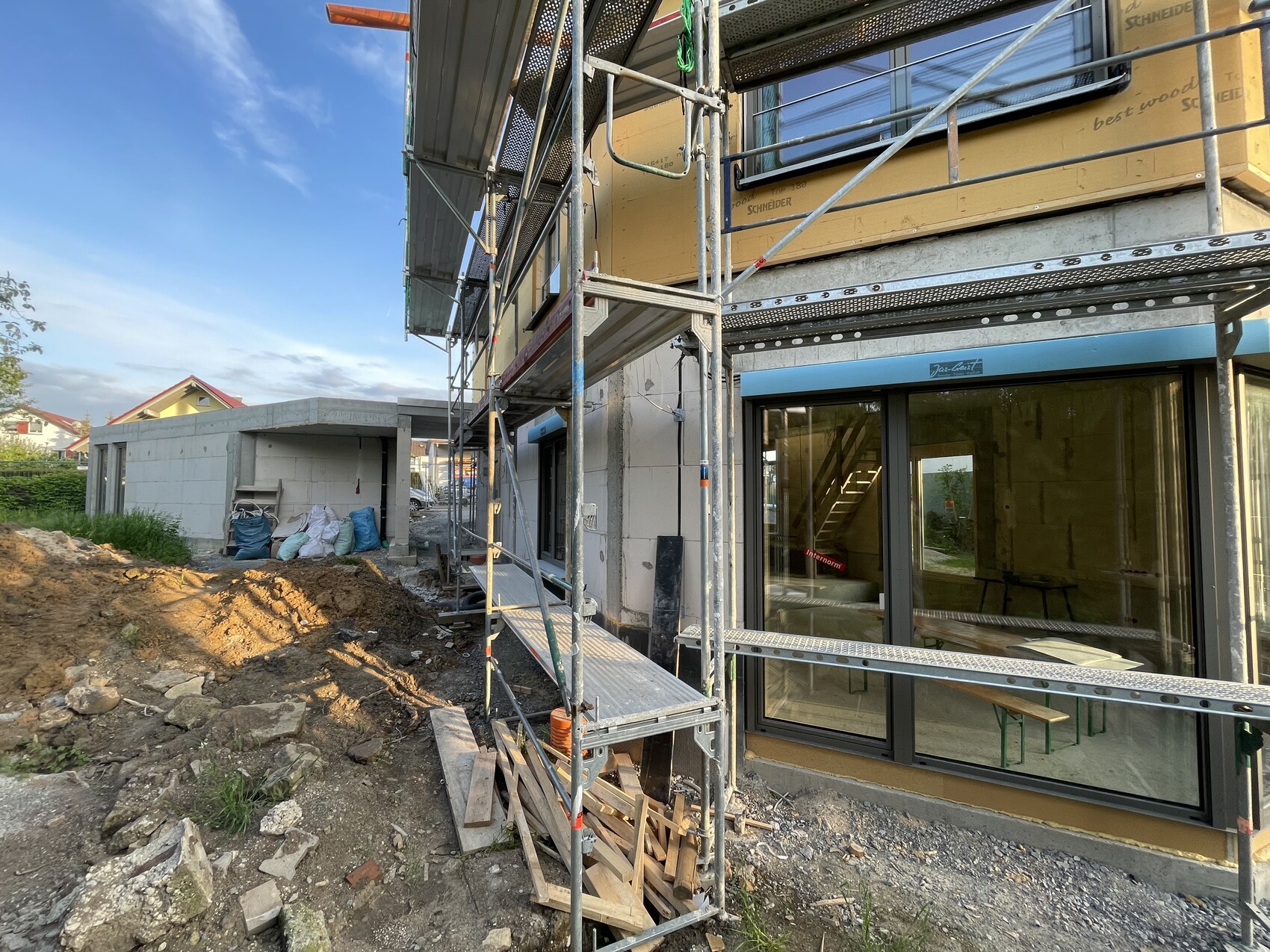 Baustelle am Wohnhaus: Gerüst um gelbe Fassade, große Fensterfronten und Baumaterialien.