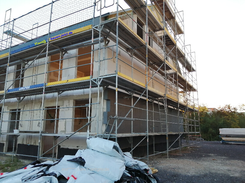 Rohbau eines Hauses umgeben von Gerüstbau, Baustellengeräten und Baumaterialien.