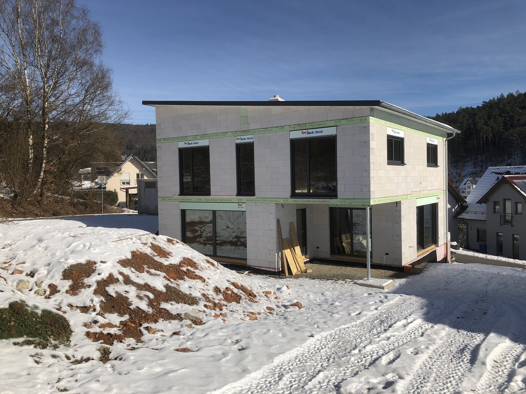 Neubau eines zweistöckigen Hauses mit großen Fenstern, Bauholz vor Eingang, Schnee.