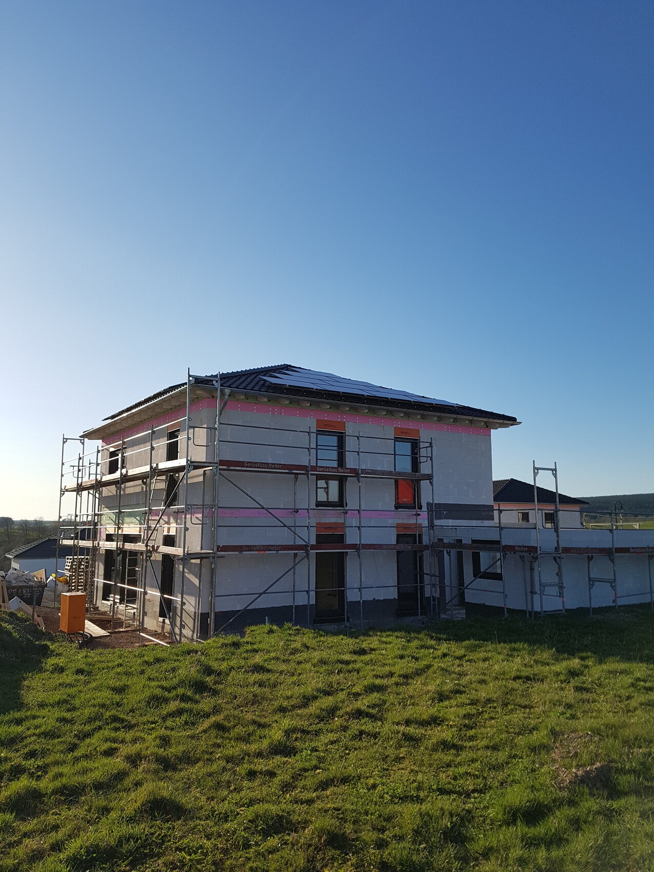 Neues Wohnhaus im Bau mit Gerüst, grüne Wiese und klarer blauer Himmel