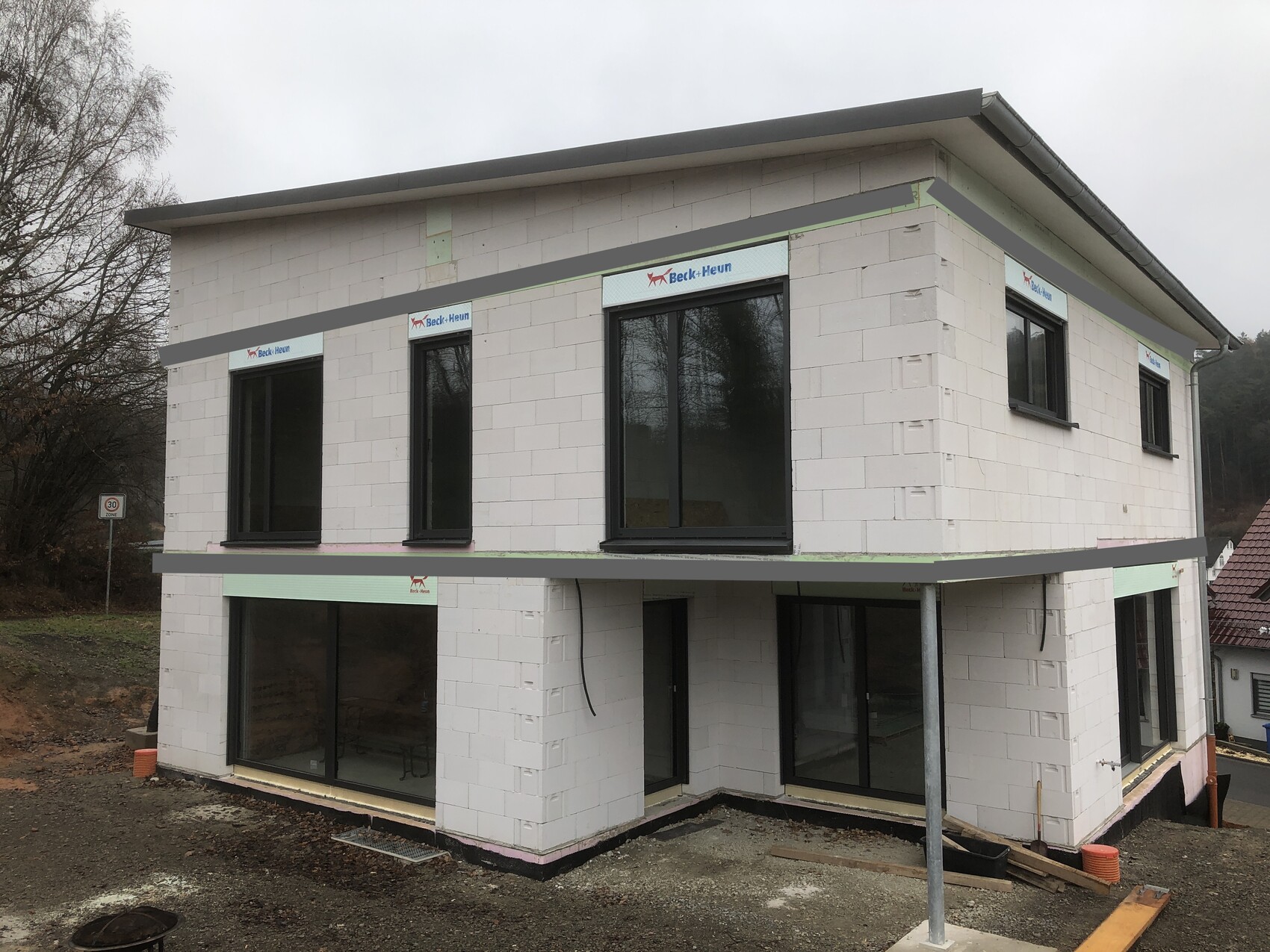 Modernes zweistöckiges Neubauhaus mit großen Fensterfronten auf einer Baustelle.