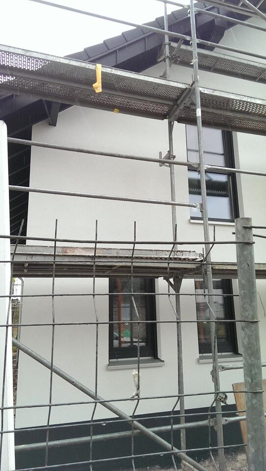 Baustellengerüst vor einem modernen weißen Haus mit Fenstern; Bauarbeiten sichtbar.
