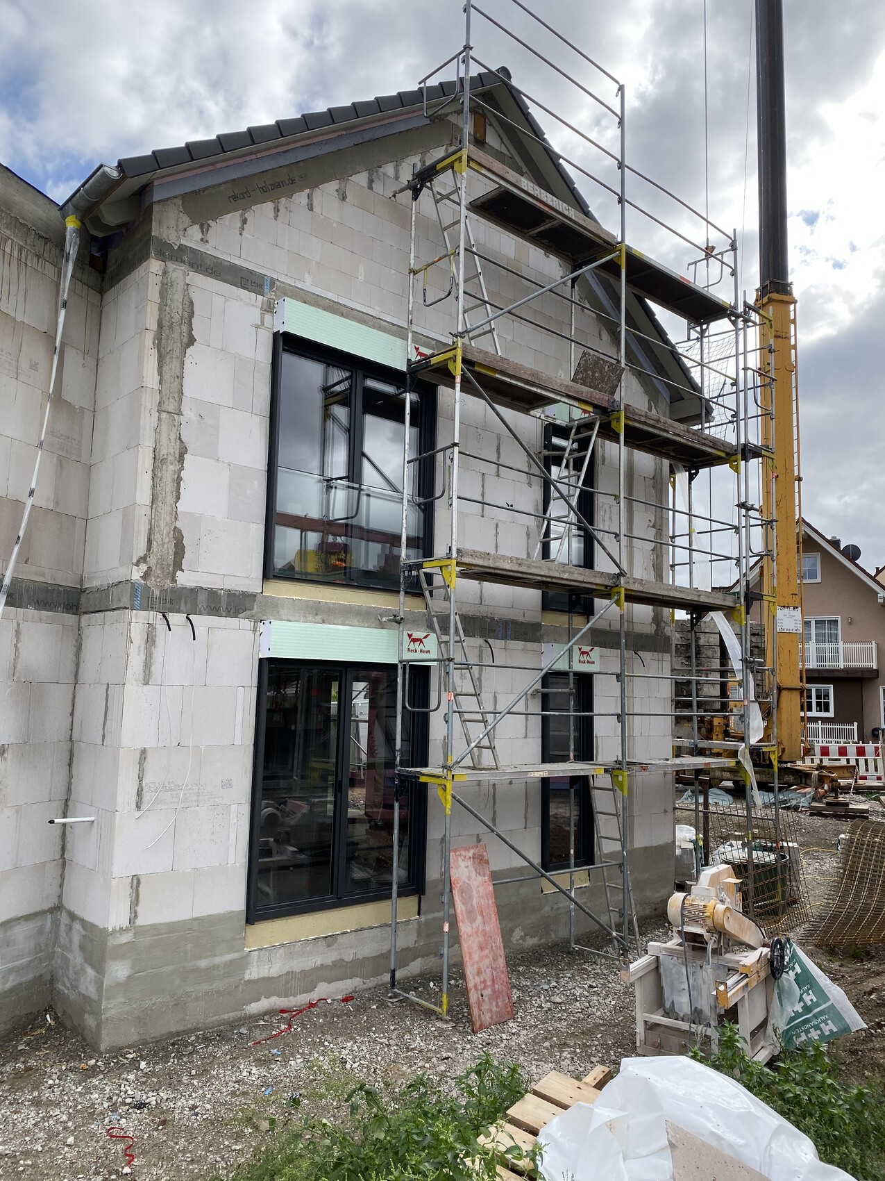 Mehrfamilienhaus im Rohbau mit Gerüst, Fenstern und Baumaterialien auf der Baustelle.