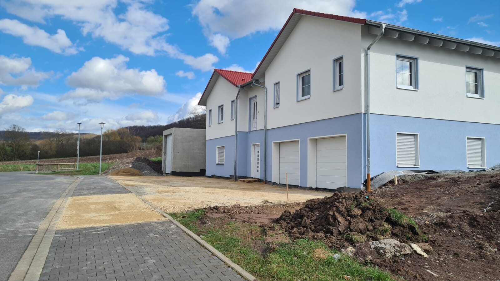 Neubau-Haus mit Garage, zweistöckige weiße Fassade, blaues Unterteil, Baustelle