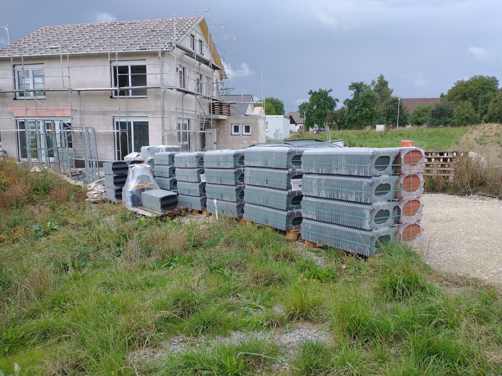 Baustelle: Rohbau mit Gerüst; davor gestapelte Betonbauteile auf Paletten.