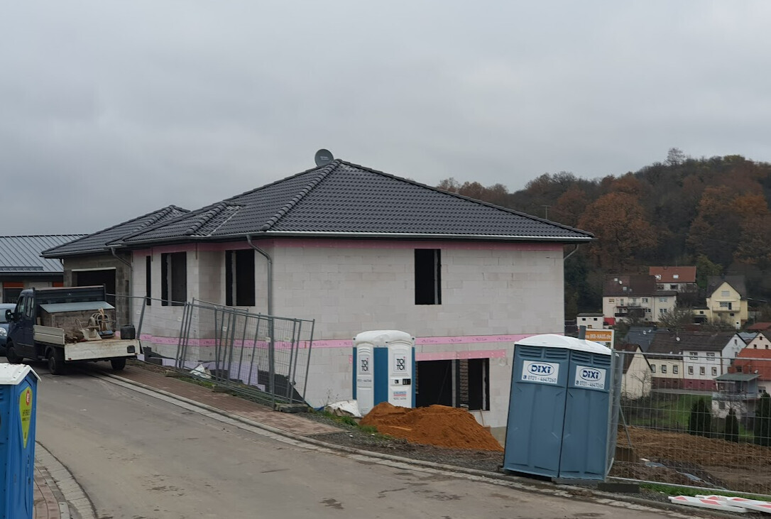 Unfertiges zweistöckiges Neubauhaus mit Baugeräten, Zaun und Porta-Potties.