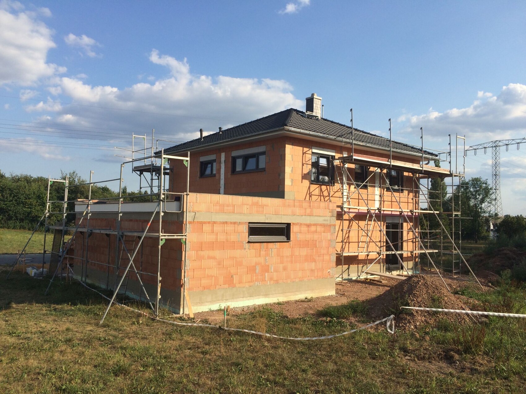 Ziegelrohbau eines zweigeschossigen Hauses mit Gerüsten und Dacharbeiten.