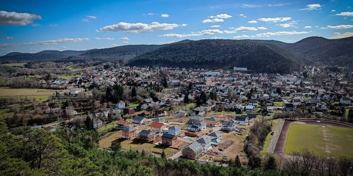Luftaufnahme eines Vororts mit Neubauten, Hügeln im Hintergrund und Sportplatz