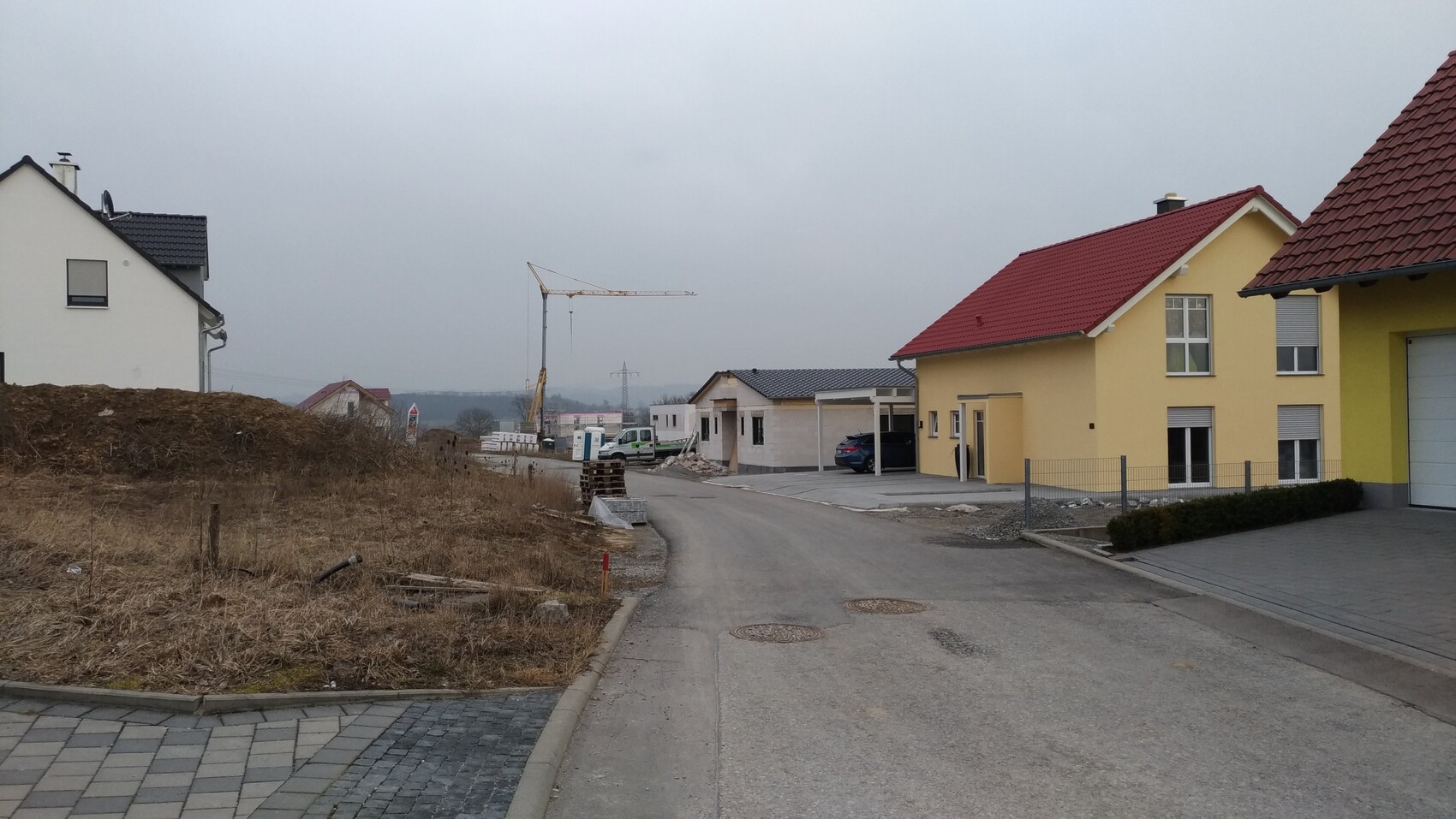 Baugebiet mit gelben Häusern, Kran auf Baustelle und unbefestigte Straße
