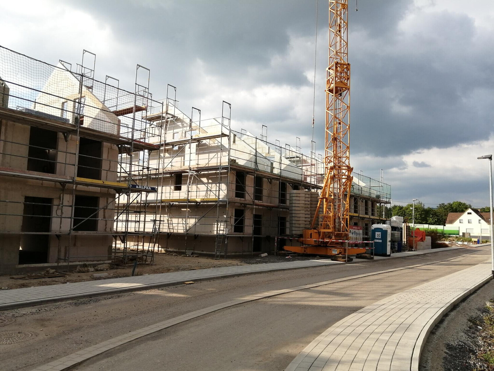 Mehrstöckiges Bauprojekt mit Gerüst, Kran und Baucontainern am Straßenrand.
