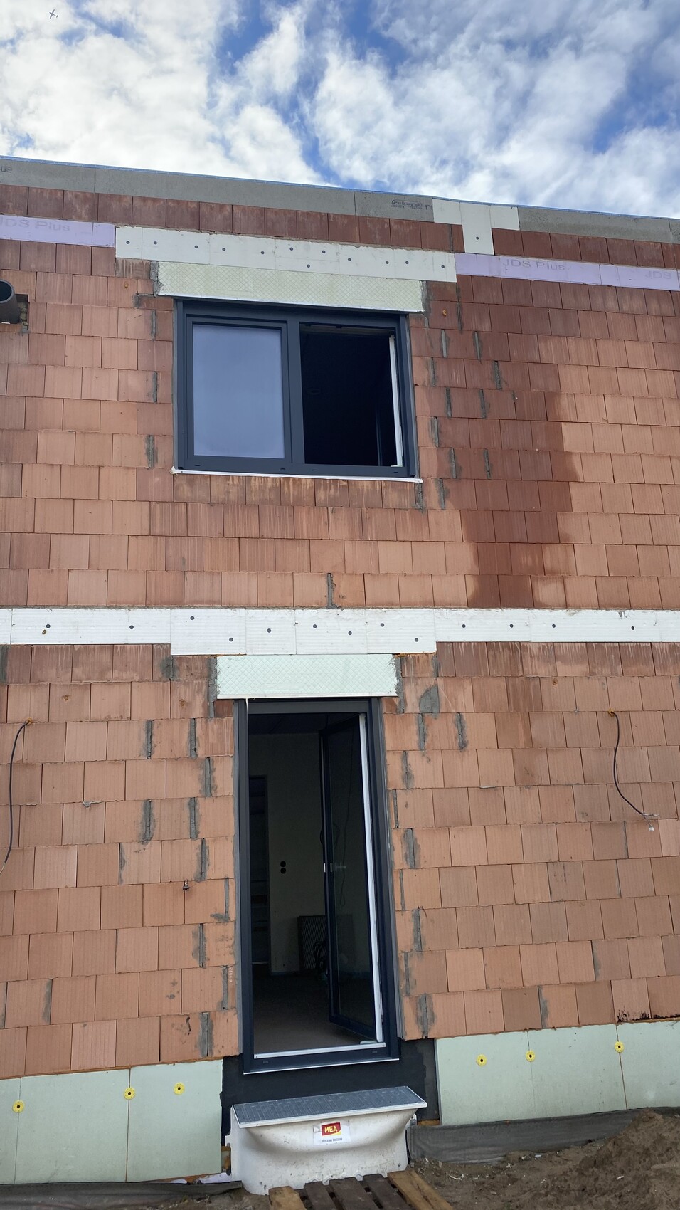 Außenfassade aus roten Ziegeln mit offener Tür unten und Fenster oben, Wolkenhimmel.