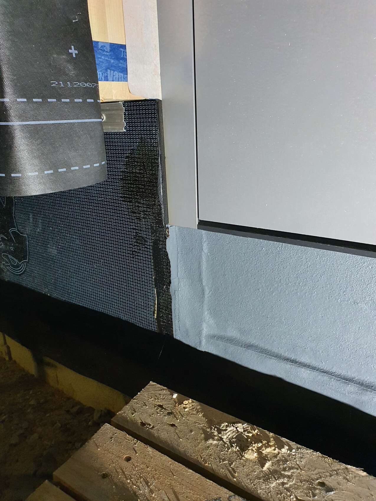 Außenwand im Bau: Dämmmaterial, schwarze Dampfbremse mit Muster, graue Fassadenpaneele.