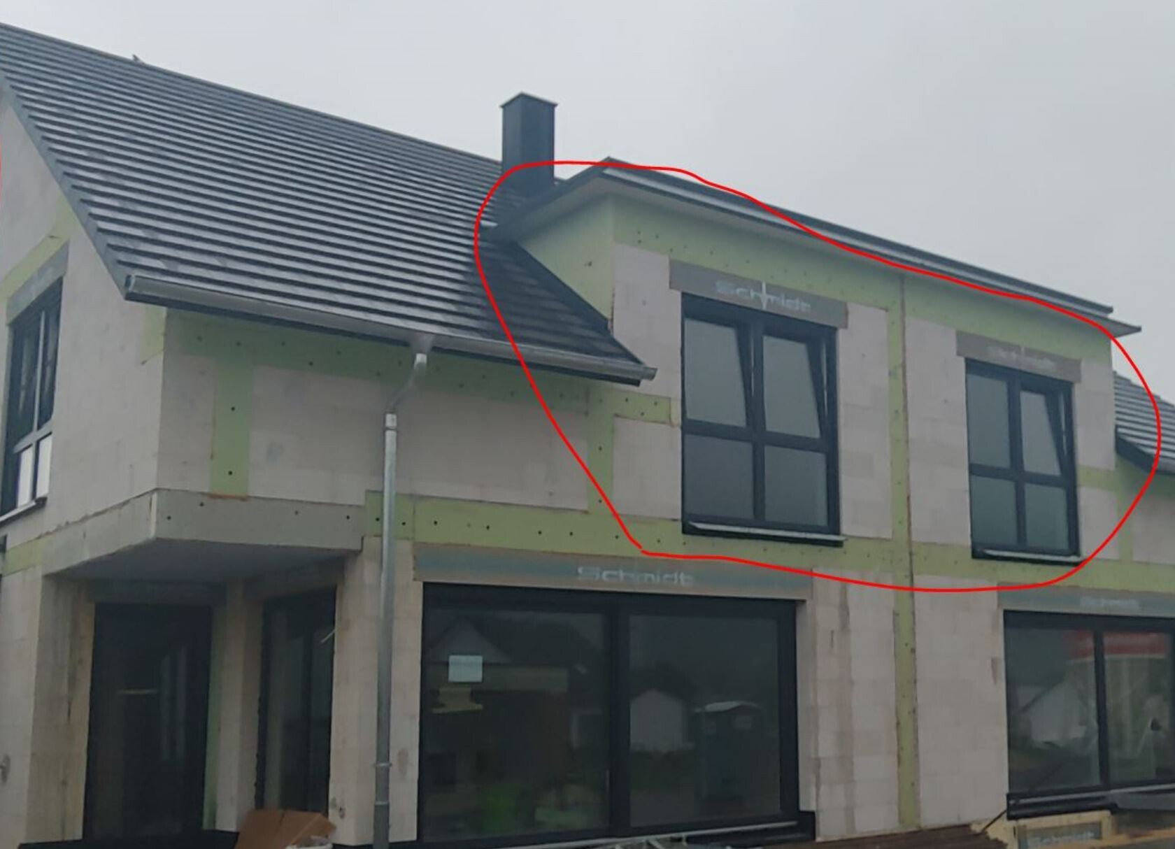 Gebäude im Bau: grüne Dämmplatten, große Fensterelemente mit schwarzen Rahmen, dunkles Ziegeldach.