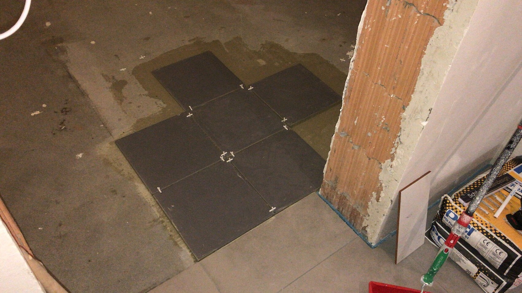 Dunkle quadratische Bodenfliesen werden verlegt, Fliesenabstandshalter sichtbar, Baubereich.