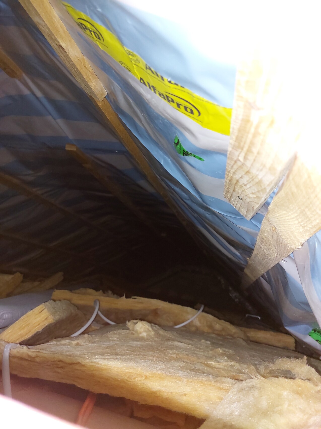 Dachboden mit Holzbalken, gelber Glaswolle-Isolierung und blauer Dampfsperre
