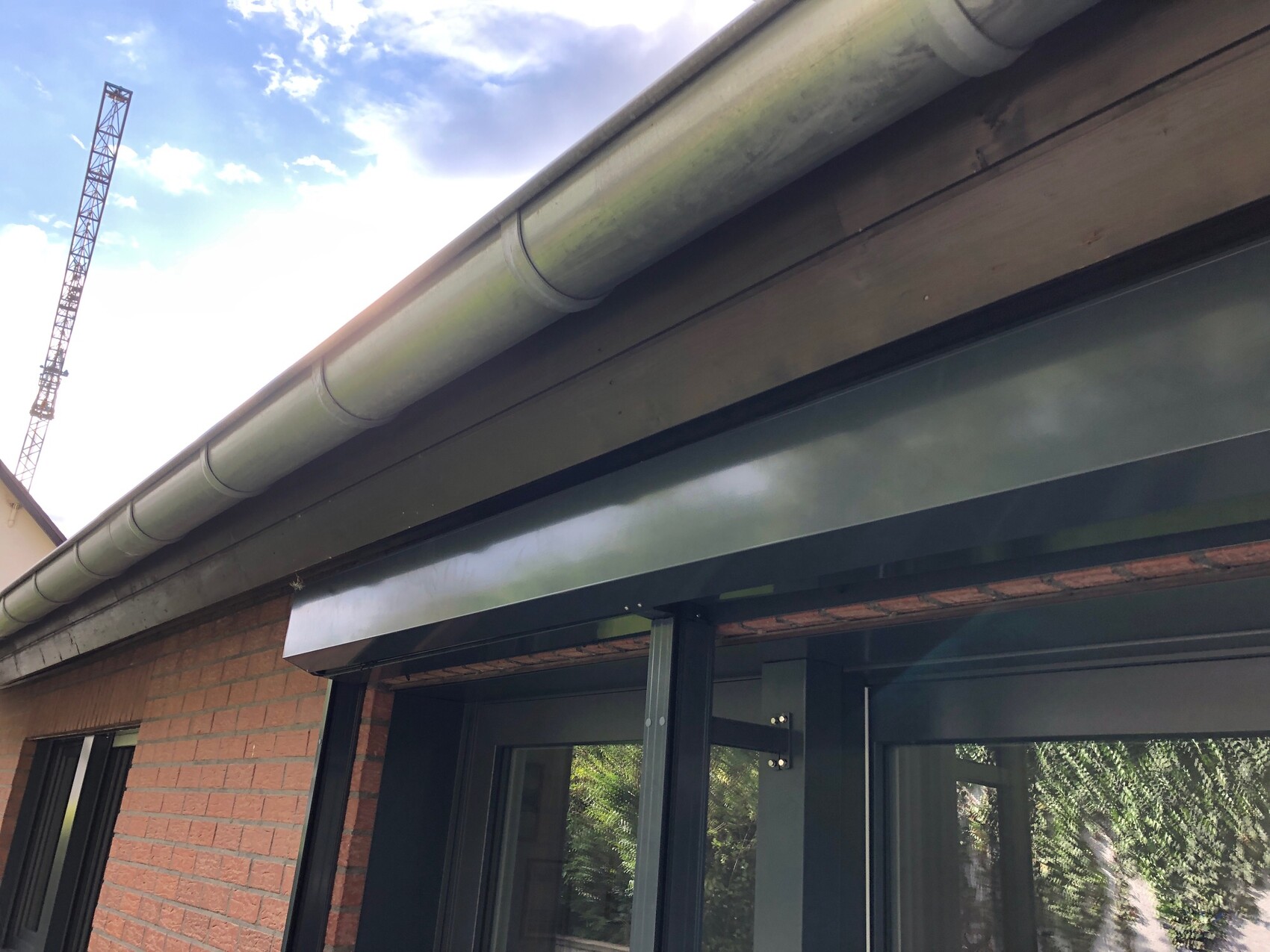 Außenansicht eines Ziegelhauses mit Dachrinne aus Metall; Baukran im Hintergrund.