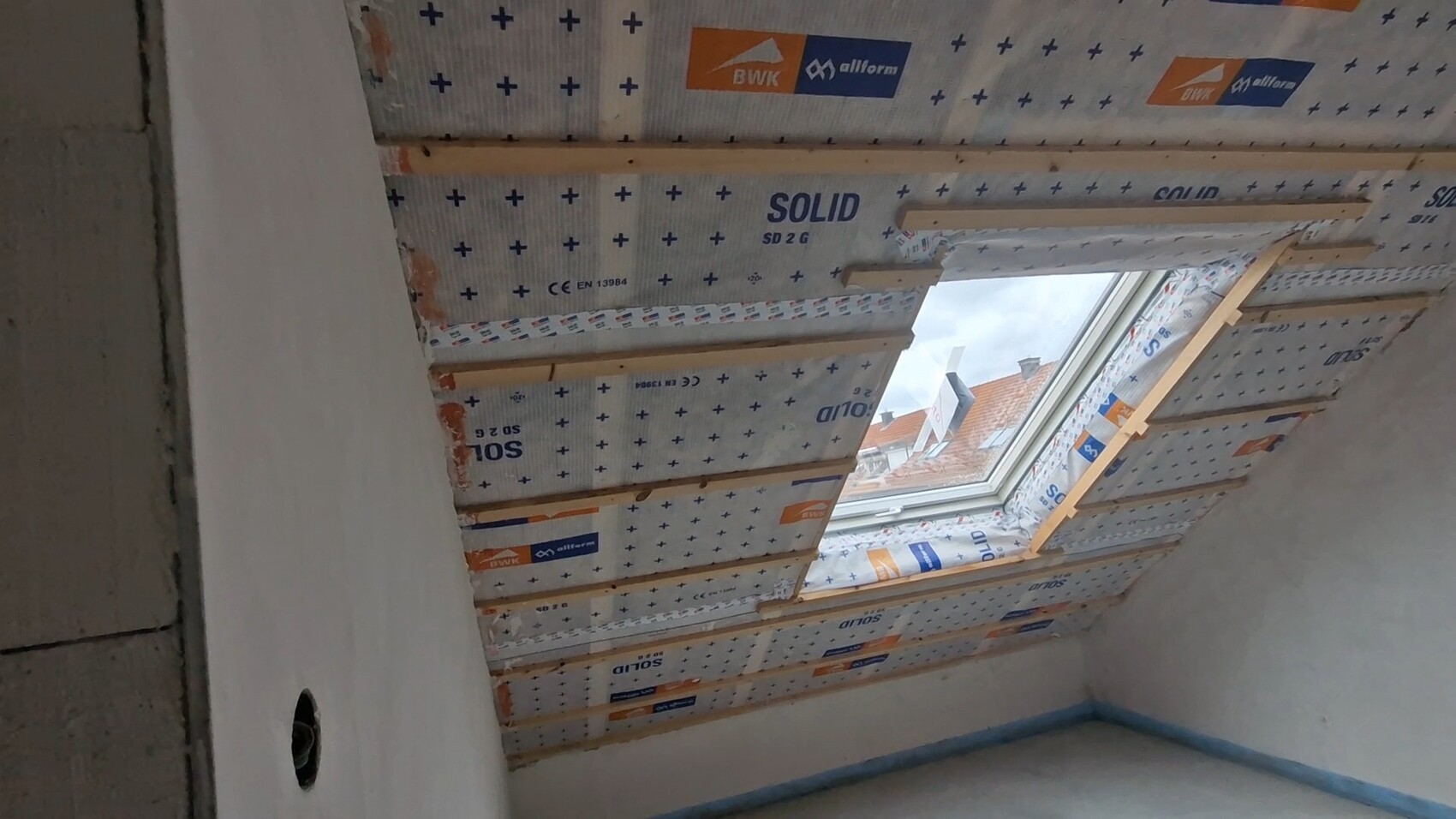Dachgeschoss mit schräger Dämmung: Dachfenster, Holzbalken und gedämmte Dachflächen.