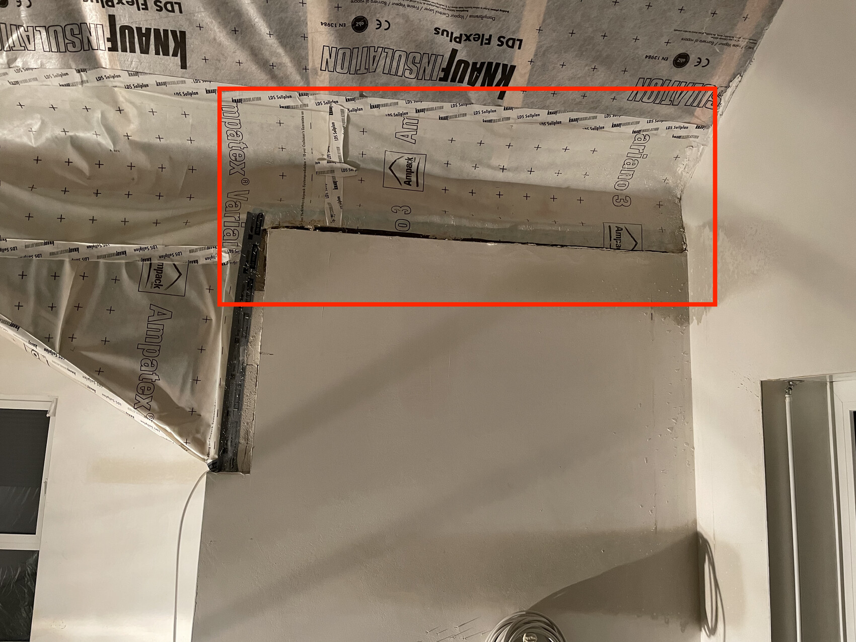 Bau- und Renovierungsbereich: Decke mit Dämmfolie, teilweise fertige Wand und lose Kabel.
