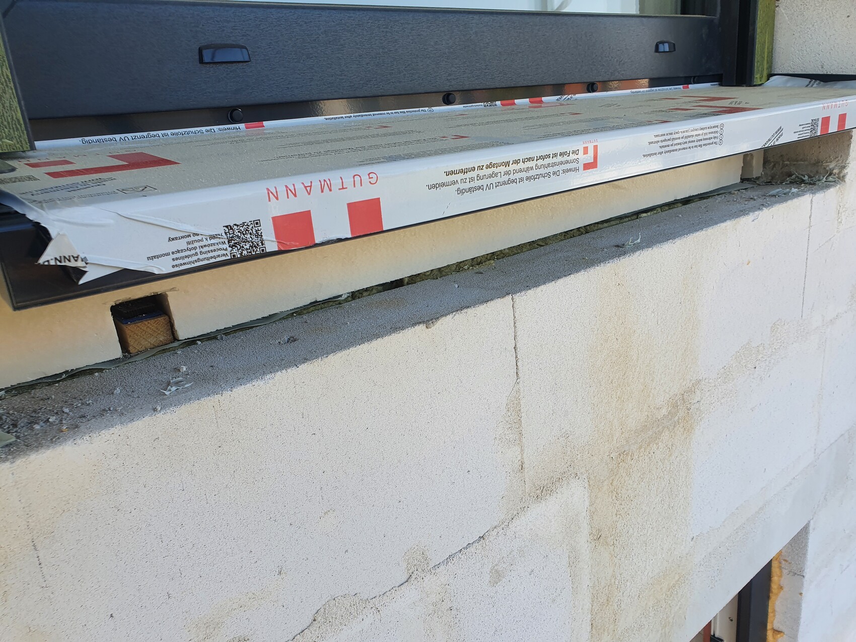 Fensterrahmen installiert über einer Beton-Mauer; verpackte Dämmung liegt auf der Öffnung.