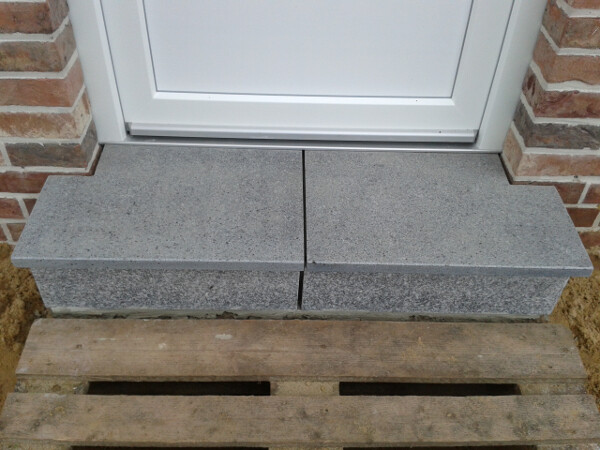 Neue graue Betonstufen vor Haustür mit Backsteinwand