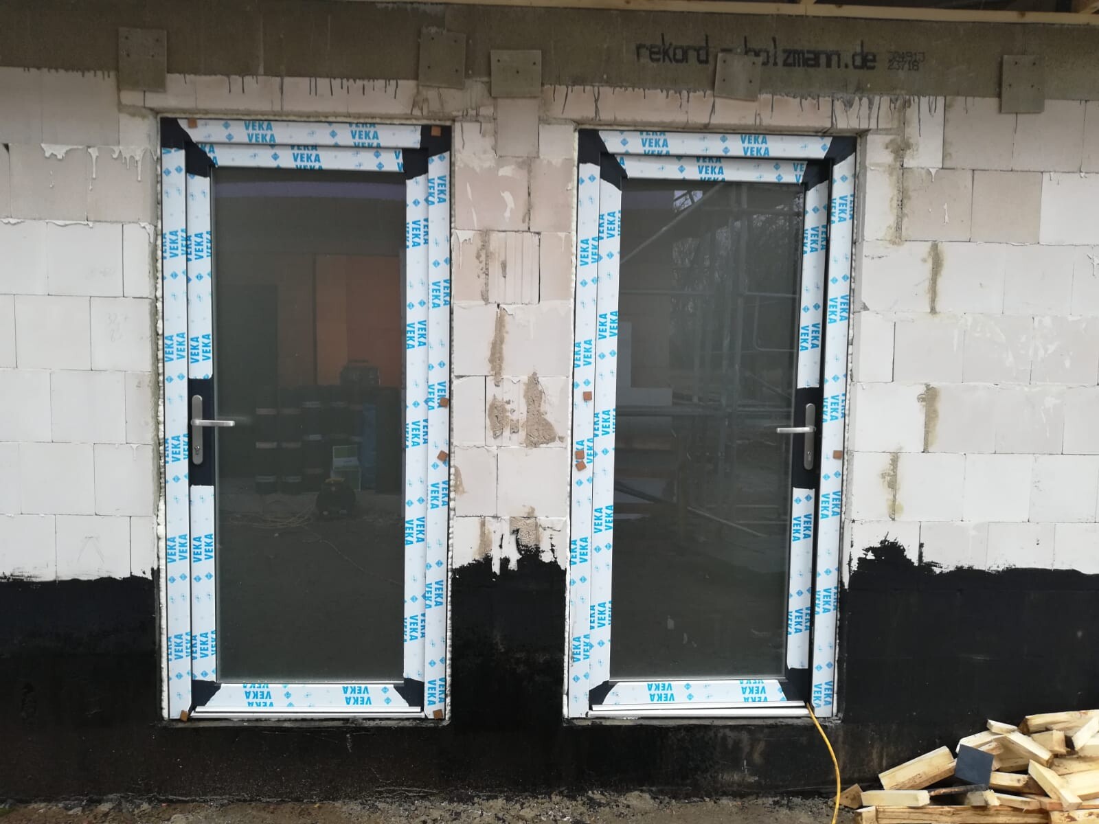 Zwei Glastüren im Rohbau, VEKA-Verpackung umrahmt die Rahmen, Holzreste rechts.