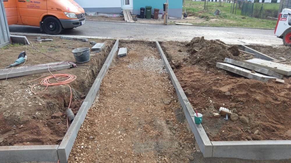 Baustelle mit ausgehobenen Gräben, Betonfundamenten, Bauwerkzeug und Van im Hintergrund