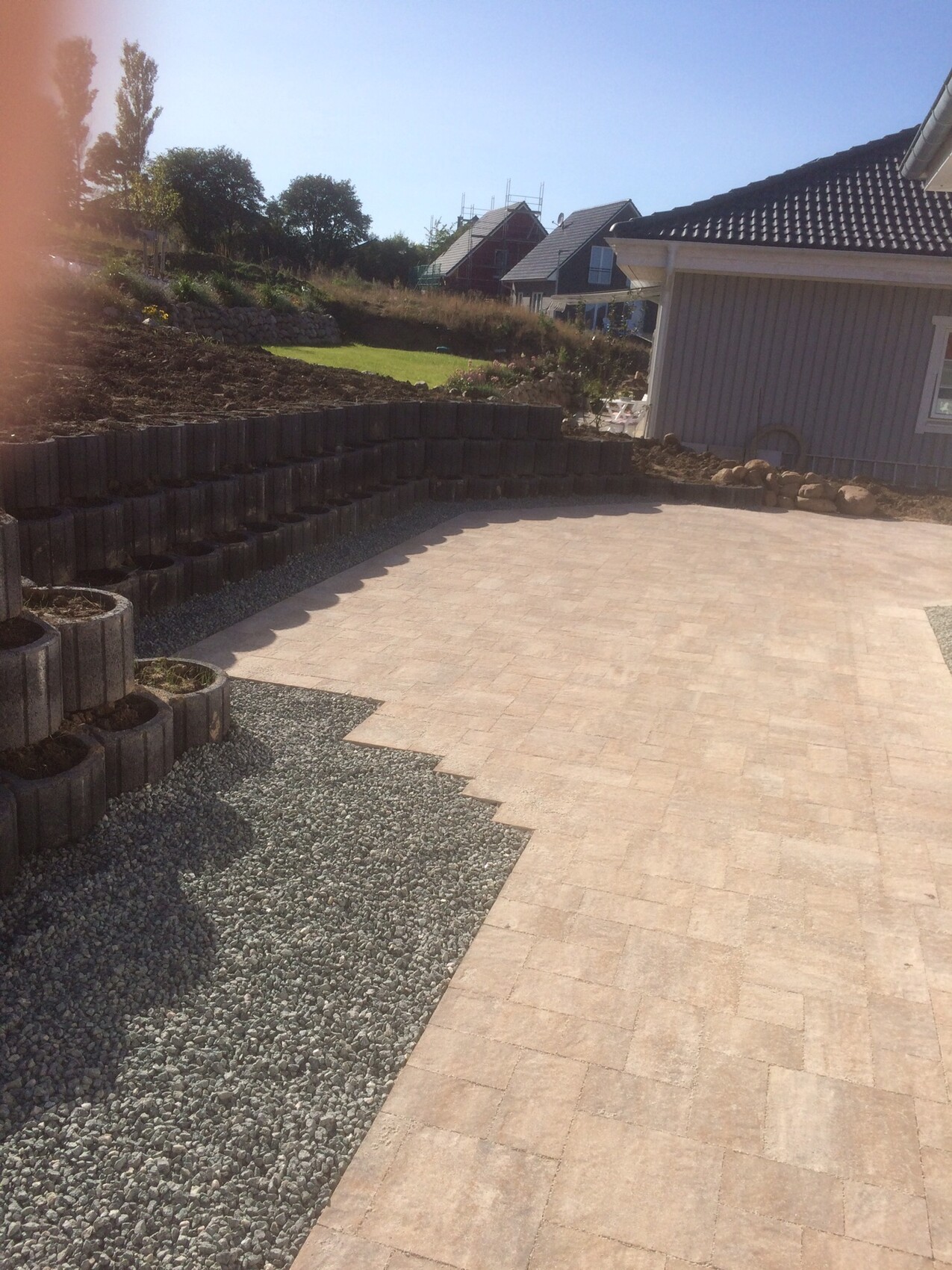 Gepflasterte Terrasse mit Kiesbereich, Stützmauer aus Blöcken und angrenzendem Haus