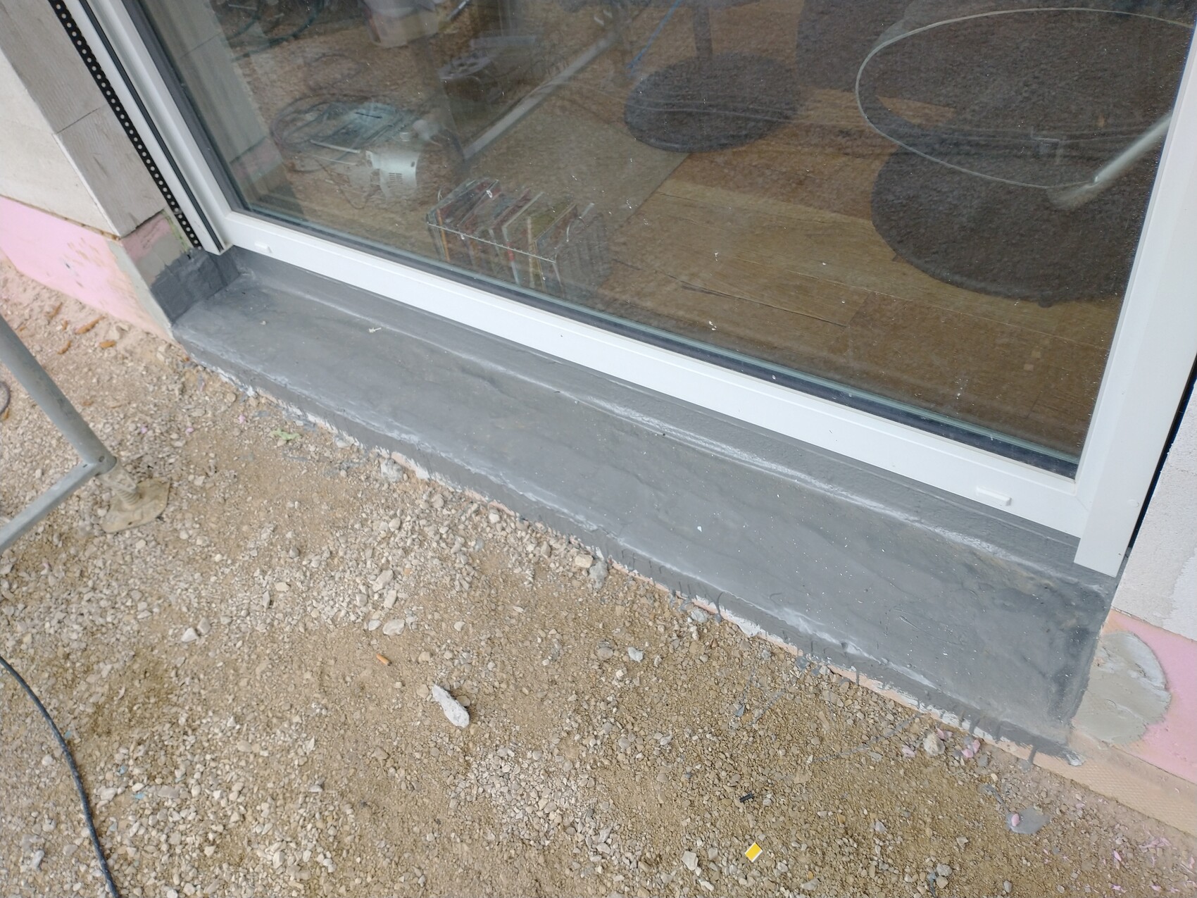 Glas-Tür mit grauer Beton-Schwelle; Baugrund davor, Innenraum sichtbar.