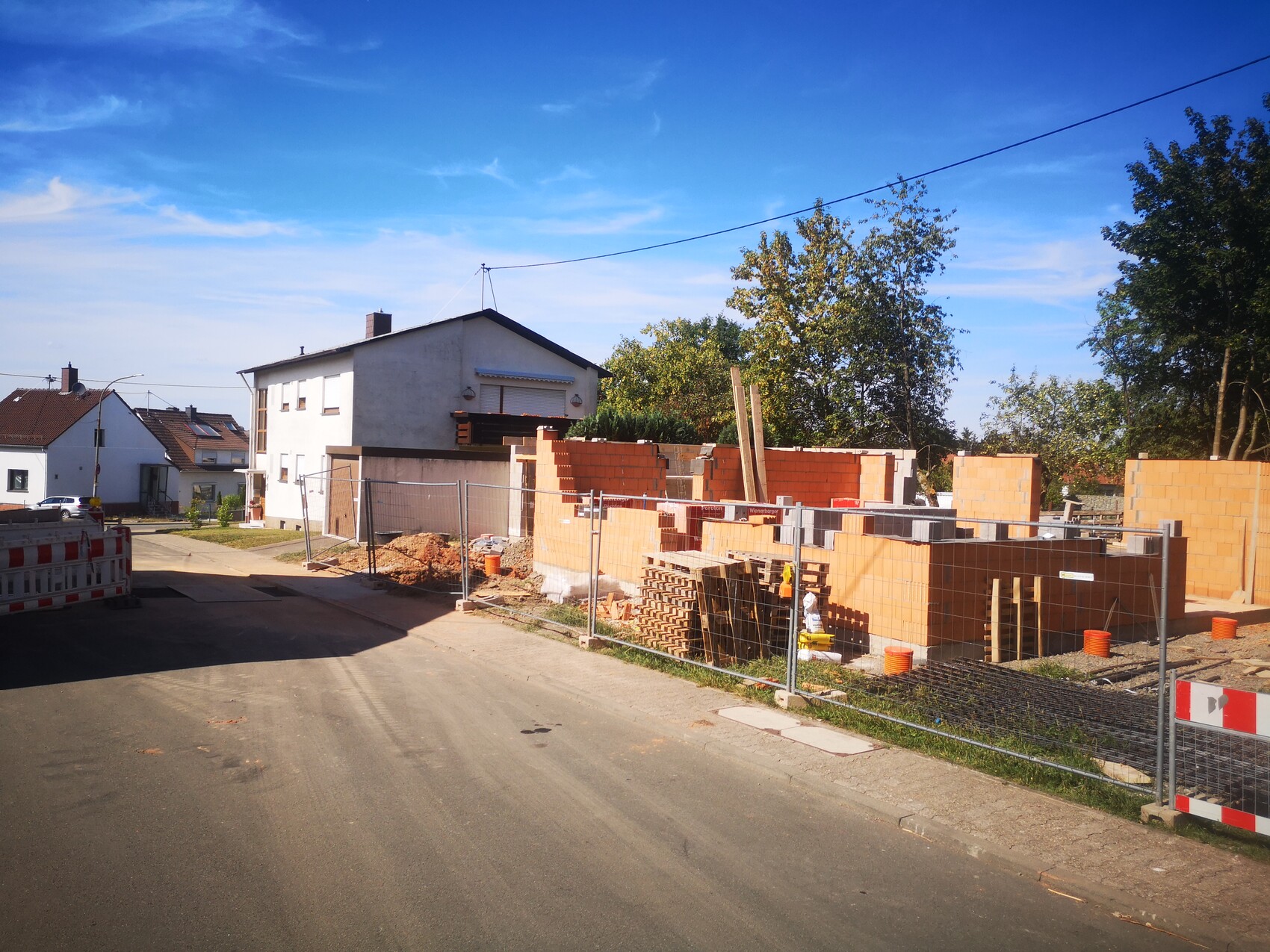 Baustelle in Wohnviertel: orange Ziegelwände, Bauzäune, weißes zweistöckiges Haus im Hintergrund.