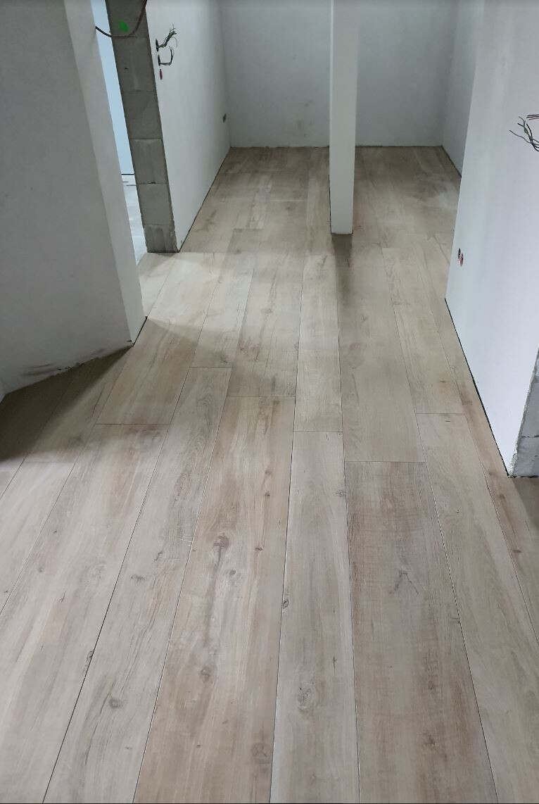 Heller Holzfußboden in einem unfertigen Innenraumflur mit weißen Wänden und Stützbalken.