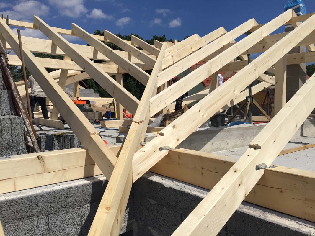 Holz-Dachkonstruktion aus Trägern auf Betonfundament; Bauarbeiter im Hintergrund.
