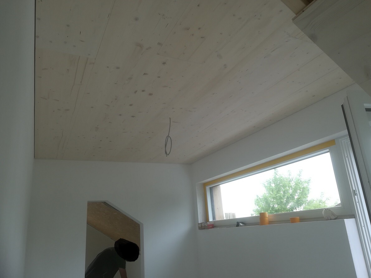 Baustellenraum: Holzdecke, Kabel, Person in Türöffnung, Fenster nach draußen.