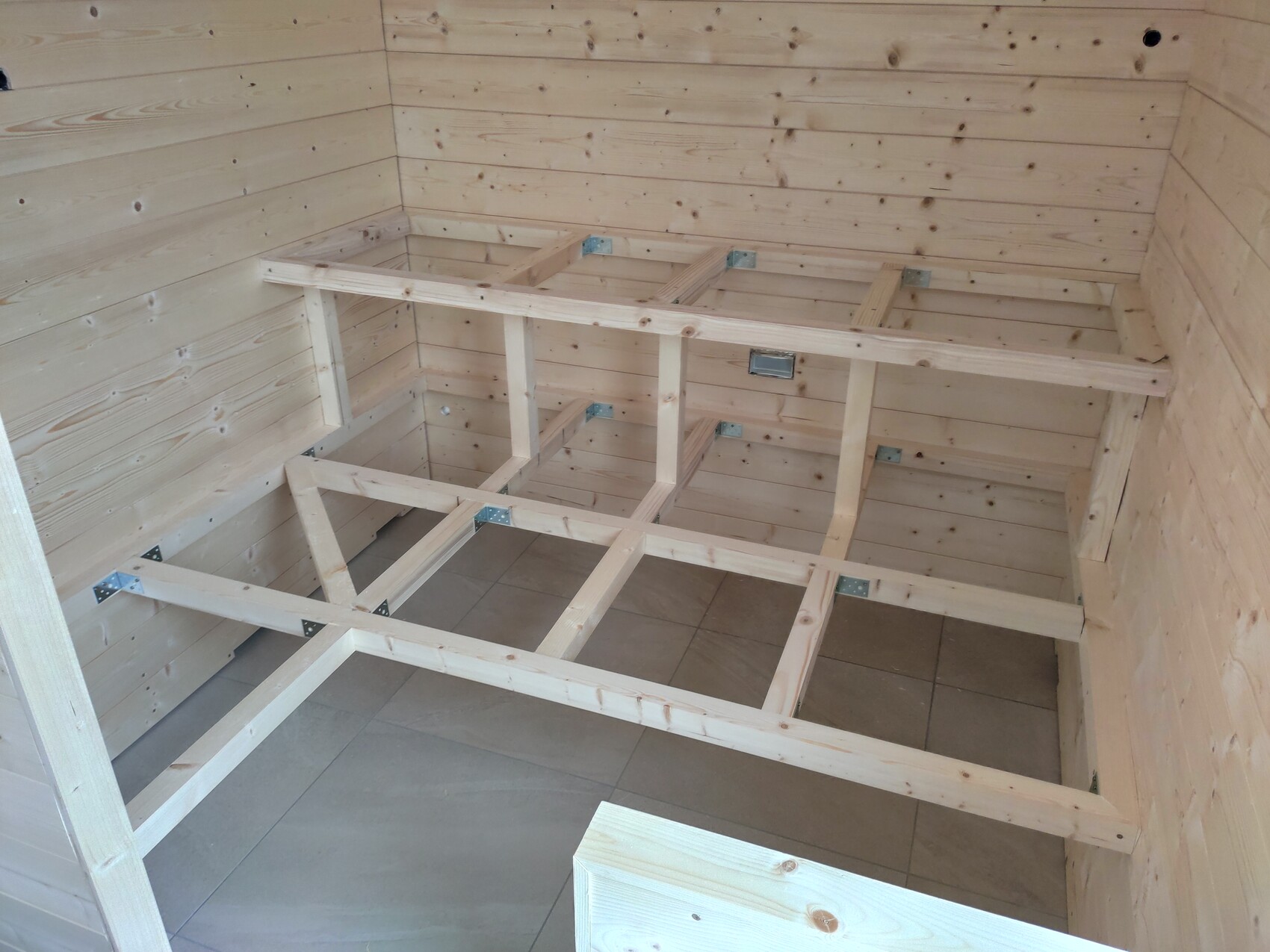 Unfertiger Holzbett-Unterbau aus Balken mit Metallwinkeln im Innenraum.