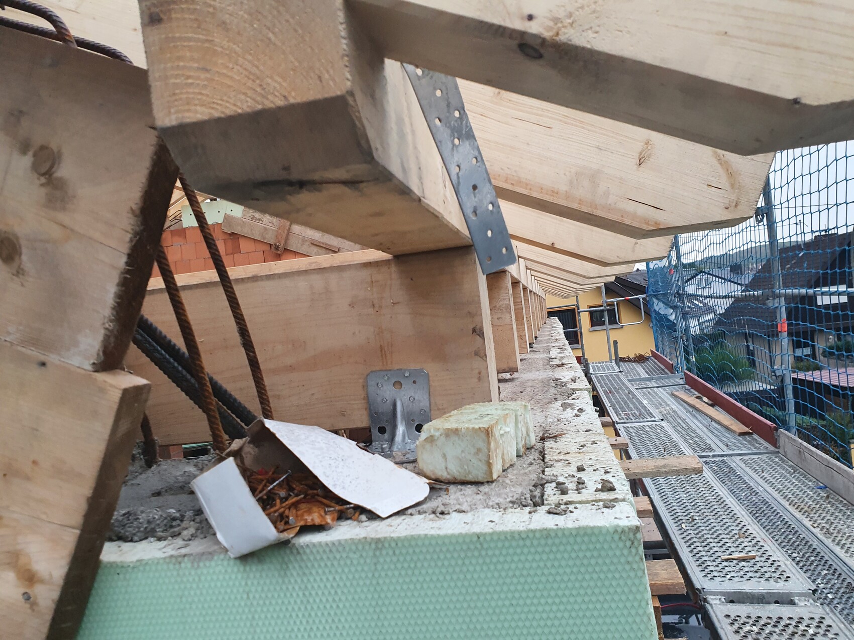 Baugerüst mit Holzformwerk, Edelstahlbewehrung und Bauschutt auf einer Plattform.