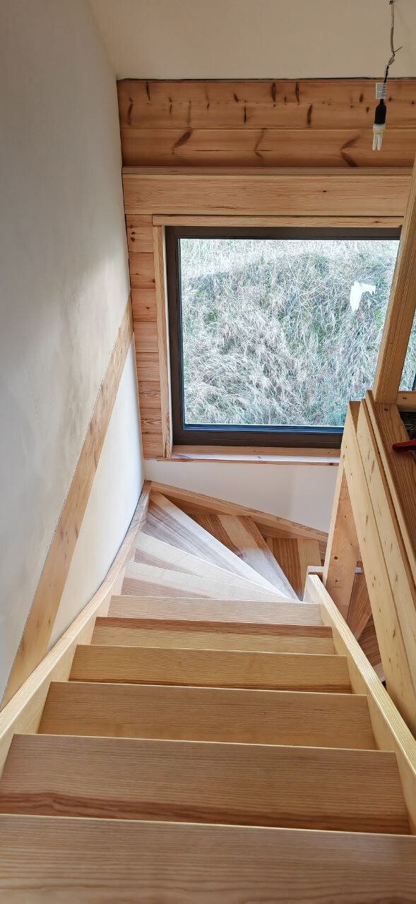 Holztreppe im Bau mit Fenster am Treppenabsatz und freiliegende Glühbirne