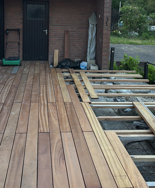 Holzterrasse wird vor einem Ziegelhaus verlegt; Dielen liegen auf der Unterkonstruktion.