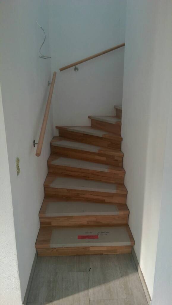 Holztreppe in einem Treppenhaus, seitliche Geländer aus Holz, unfertige Wände im Hintergrund